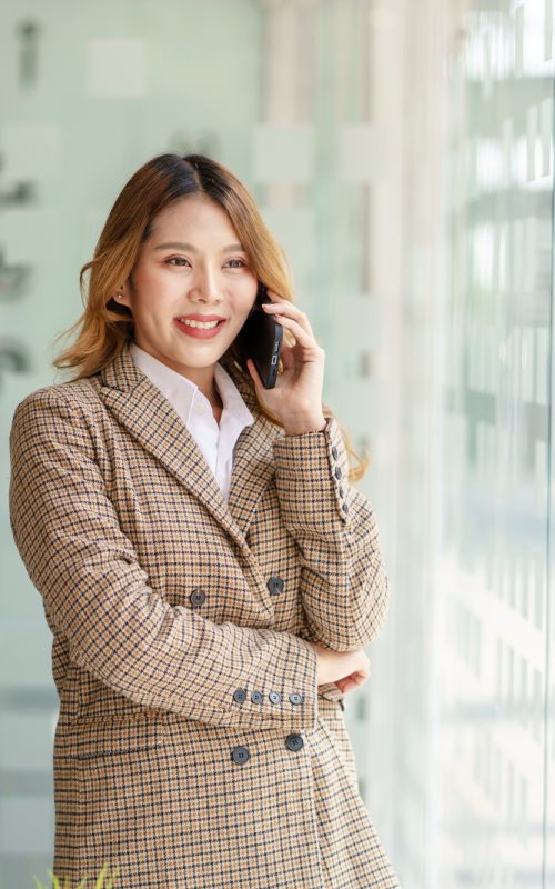 Pretty young Asian business woman standing talking on the phone in the office.